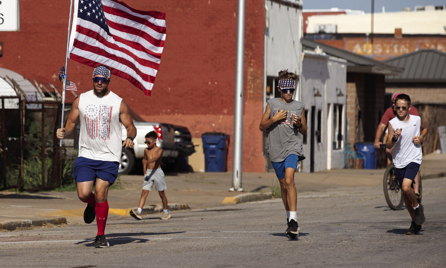 Runners carrying American flags make their way through downtown Guthrie during the seventh annual Freedom Ride on July 4. Photo by Brent Fuchs