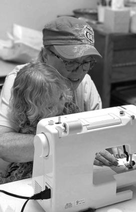 Noble thread member sewing parts of a quilt with one of the youngest members assisting.