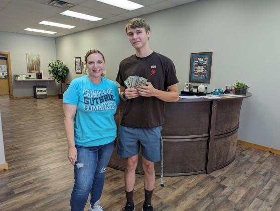Brittany Timmons, President and CEO of Guthrie Chamber of Commerce presents $1000 cash to Guthrie Alum Logan Hand.