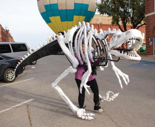 A towering dinosaur roams downtown Guthrie on Halloween, with a hot air balloon providing a dramatic backdrop for trick-or-treaters.