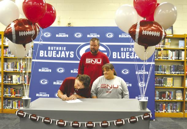 Guthrie senior Jace Rainwater signs to continue his football career at Southern Nazarene University while surrounded by his parents during a signing ceremony at Guthrie High School. Rainwater, the class valedictorian, was a standout wide receiver for the Bluejays. Photo by Nikki Bos