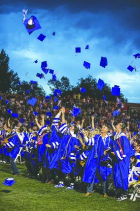 With storm clouds looming overhead, graduates celebrate during the traditional hat toss at Guthrie High School’s 2026 commencement ceremony. Photo by Brent Fuchs.