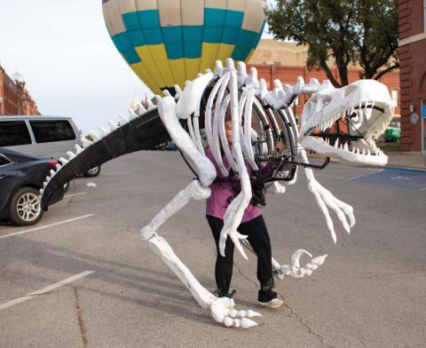 A towering dinosaur roams downtown Guthrie on Halloween, with a hot air balloon providing a dramatic backdrop for trick-or-treaters.