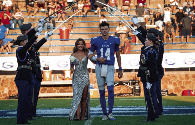 Guthrie’s Daelon Rice, No. 14, escorts a Homecoming Queen Megan Mefford beneath a saber arch held by JROTC cadets before the Bluejays’ Homecoming game against Blanchard at Jelsma Stadium Friday, Sept. 18. The traditional saber arch was part of the evening’s Homecoming festivities as students, families and fans gathered to celebrate “Jurassic Jays” and cheer on the Bluejays.  Photo by Reece Heck 