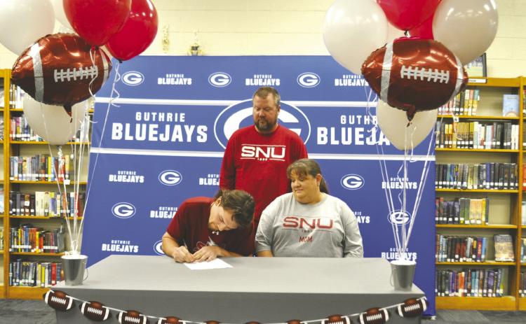 Guthrie senior Jace Rainwater signs to continue his football career at Southern Nazarene University while surrounded by his parents during a signing ceremony at Guthrie High School. Rainwater, the class valedictorian, was a standout wide receiver for the Bluejays. Photo by Nikki Bos